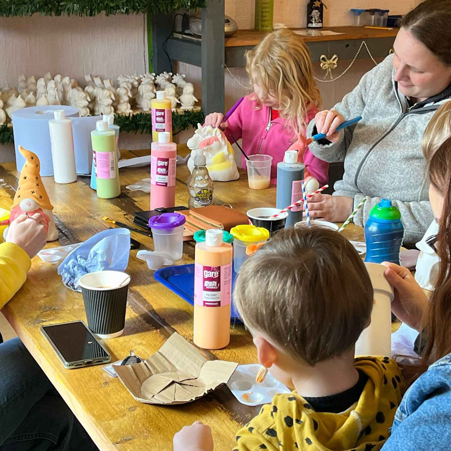 Children and family joyfully painting pottery ceramics at a bright sunny craft workshop studio