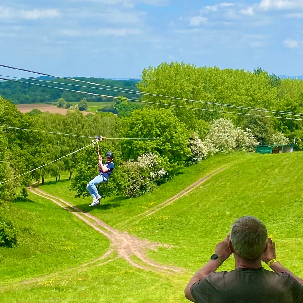 Excited smiling child wearing a safety helmet and harness riding a scenic 100-meter zip wire over lush green woodland trees in the English countryside, sunny bright day, adventure park, high quality action lifestyle photography